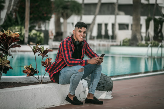 Ethnic Man With Smartphone Sitting On Poolside