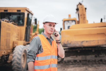 Portrait of caucasian engineers using smartphones in the workplace. Engineers wear helmets and use...