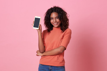 Naklejka premium Portrait of happy young african woman showing at blank screen mobile phone isolated over pink background.