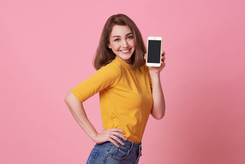 Portrait of happy young woman showing at blank screen mobile phone isolated over pink background.