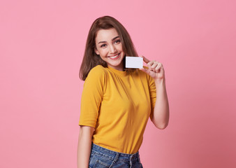Portrait of a young woman in yellow shirt showing credit card and looking away at copy space...