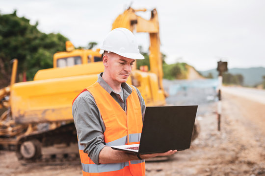 Caucasian Young Engineer Using A Laptop On Road Construction Site. Engineer Work Concept