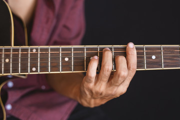 Close-up of man's hands playing acoustic guitar on black background