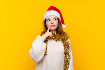 Girl with christmas hat over isolated yellow background thinking an idea