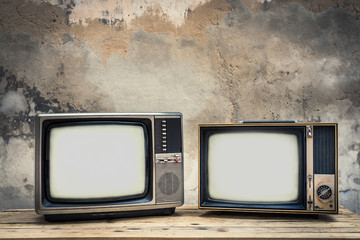 Two old television on wood table with old concrete wall background. Vintage TV filter tone. Retro style