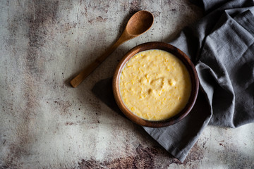 Mouthwatering corn porridge in stylish wooden bowl with beautiful wooden spoon on vintage grey background