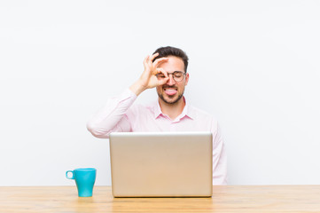 young handsome businessman smiling happily with funny face, joking and looking through peephole,...
