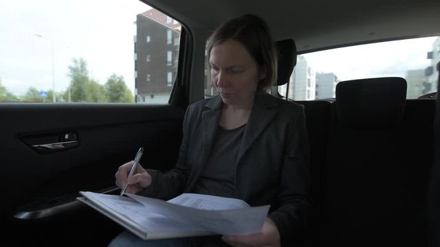 Businesswoman doing paperwork in car at the back seat