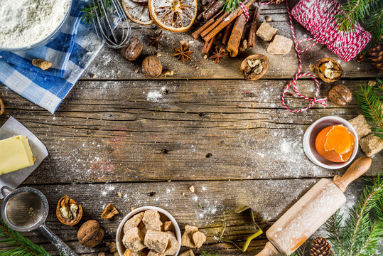 Christmas baking background with utensils and ingredients - flour, eggs, brown sugar and spices. With christmas decorations and fir tree on rustic wooden background, top view with copy space.