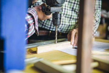 Unrecognizable senior couple drilling a wooden batten in their workshop