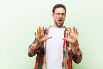 young handsome man feeling terrified, backing off and screaming in horror and panic, reacting to a...