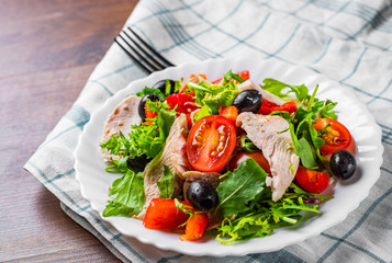 Fresh salad with chicken breast, arugula, black olives,red pepper, lettuce, fresh sald leaves and tomato on a white plate on wooden table background