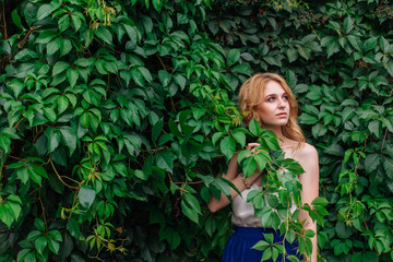 Portrait of a young beautiful woman, standing next to the wall of wild grape leaves.