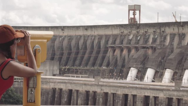 Hispanic woman using coin operated binoculars to see the Itaipu Dam. 4k
