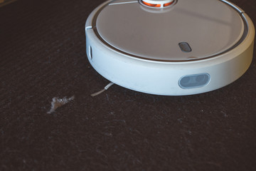 Robotic vacuum cleaner working on floor. Removes dust from the brown carpet