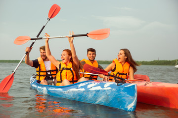 Happy young caucasian group of friends kayaking on river with sunset in the backgrounds. Having fun...