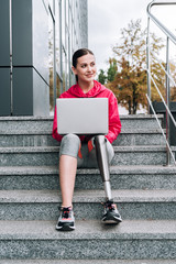 disabled sportswoman using laptop while sitting on stairs on street