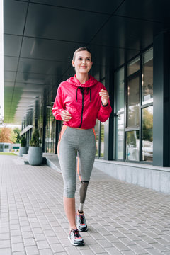 full length view of smiling disabled sportswoman running on street