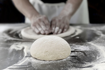 Ball of pizza dough on table with chef hands knead the dough in background.