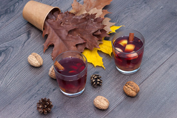 Mulled red wine with spices and fruits on a wooden table. Autumn fall leaves.
