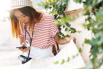 Asian woman walking outdoors using mobile phone.