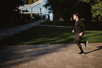 Fototapeta na wymiar Young handsome stylish sporty man on morning run in park