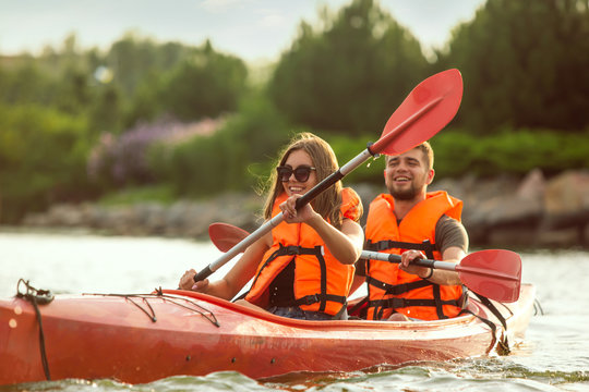 Happy young caucasian couple kayaking on river with sunset in the backgrounds. Having fun in leisure activity. Happy male and female model laughting on the kayak. Sport, relations concept. Colorful.