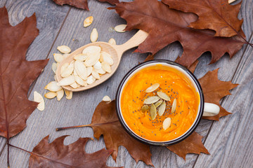 Fototapeta premium Vegetarian autumn pumpkin cream soup with seeds with autumn leaves.