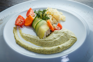 closeup rice and sliced vegetables trendy decorated with green sauce and greens served in white restaurant plate on wooden table