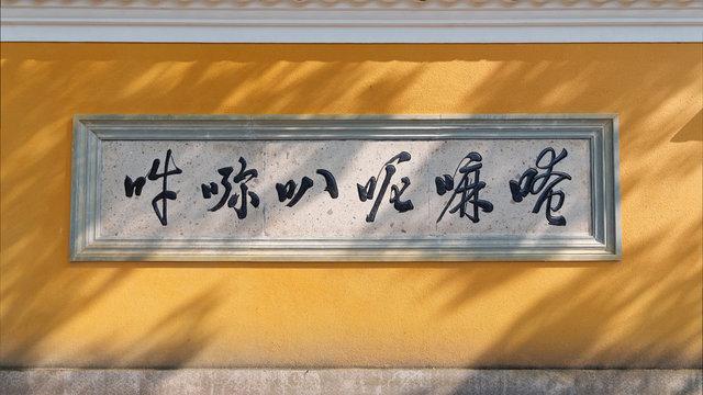 Yellow temple wall with mantra and sunny shadows, the six Chinese characters is the transliteration of Om mani padme hum.