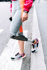 partial view of disabled sportswoman with prosthesis holding smartphone on street