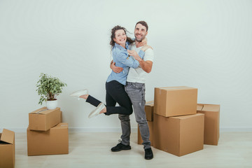 Couple moving into their new house. Woman is very glad and is hanging on her husband's neck, hugging him.