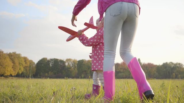 Young caucasian girl helping her little cute sister playing with a pink toy airplane. Pretty blonde child in dotted jacket running in the autumn evening.