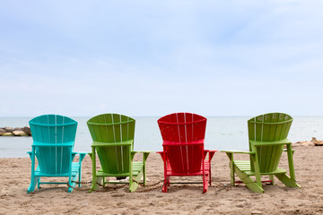 a row of colorful wooden Adirondack chairs on the beach facing the water