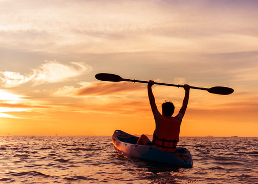 Young man kayaking on the sea at sunset