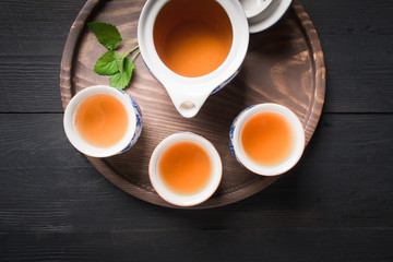 Tea ceremony. Three cup of tea with melissa and kettle on dark background. Chinese tea concept. View from above.