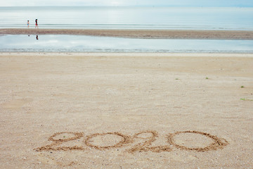Happy New Year 2020, lettering on the beach with wave and clear blue sea.
