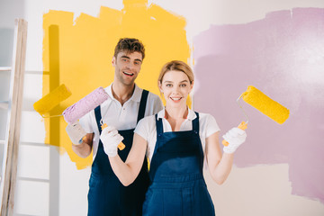 two young painters smiling at camera while holding paint rollers