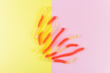 Jelly worms on a violet-yellow background. The concept of junk sweets, candies. Minimalism, top view, flat lay, place for text.