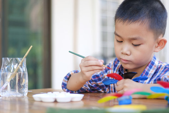 Asian boy painting a colourful plastic flower made from water bottle on wooden table outdoor.Recycled colorful plastic flowers.Recycle decoration.