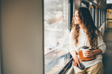 Freelancer girl in the train. Girl looking to the train window, drinking coffee and holding the...