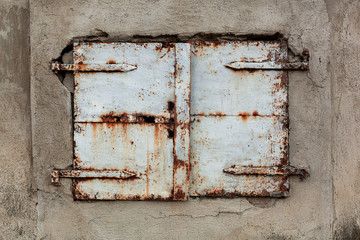 Old, rusty and weathered metal window coverings, closed shut on building exterior