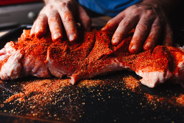 Man preparing raw piece of meat, rubbing different spices and herbs in it before roasting - obrazy, fototapety, plakaty