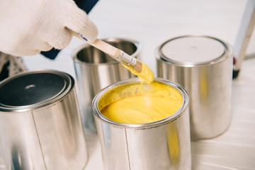 cropped view of man holding paintbrush near paint with yellow can