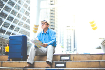 Senior man traveling with luggage sitting on staircase checking city map and sightseeing Travel and tourism concept.Elderly Travel and tourism concept.