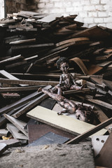 selective focus of abandoned and scary baby doll near damaged toy and wooden boards, post apocalyptic concept