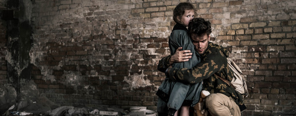 panoramic shot of handsome man hugging child near brick wall, post apocalyptic concept