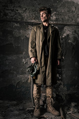 Fototapeta na wymiar handsome man standing near old wall with gas mask, post apocalyptic concept