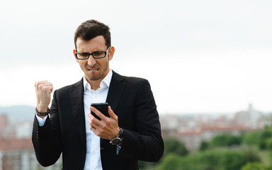 Young man doing success gesture while checking his earnings or professional goals in his smartphone.
