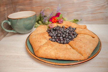 Galeta galette tart cake pie of whole grain flour with blueberries on a white country table with Turquoise color cup with flowers. Side view. Natural lighting.